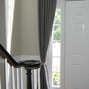 Entry way silk pinch pleated draperies puddle on floor & mounted using decorative rod and rings.