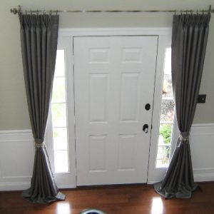 Pinch pleated silk drapes with decorative tie backs framing entryway.