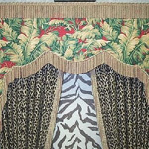 Lambrequin with bullion fringe and braided cord done in a tropical print fabric over top of a pair of pinch pleated drapery panels done in a leopard animal print fabric with the inside edge of the drapery panels trimmed in a shorter bullion fringe. The drapery panels are over top of a door that is covered in a zebra animal print fabric. The draperies are tied back with large coordinating tassel tie backs.