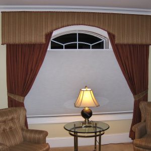 Custom cornice over arch window with tied back drapery panels and contrast reupholstered chairs