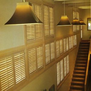 Multi-level wall of stained wooden plantation shutters in a great room ascending the stairway.