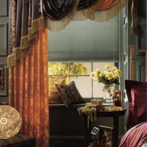 Triple swag and jabot valance with varying swag lengths and one side jabot all with bullion fringe and contrast fabrics utilizing decorative medallion hardware and large tassels, mounted over a single drapery panel.