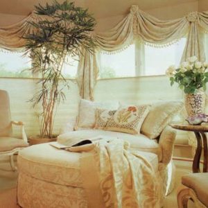 This sun room is decorated with throw swag valances with tassel fringe and rosettes over top of top down bottom up sheer shades. Also showing reupholstered skirted chair and ottoman with coordinating throw pillows and reupholstered arm chairs.