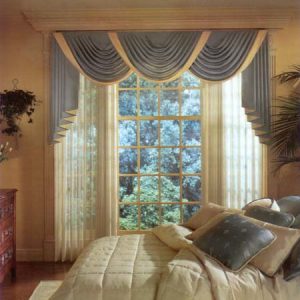 Classic swag and jabot valance done in contrast fabrics with contrast bottom edge on each of the swags. Pinch pleated sheer draperies. Box pattern quilted comforter bedding ensemble with coordinating throw pillows in coordinating fabrics.