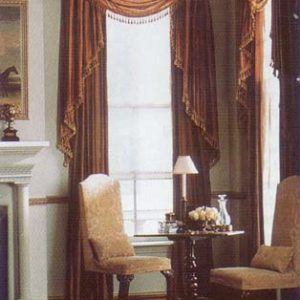 Crown royal wooden molded cornice mounted over a multi fold swag valance with unstructured jabots and decorative trim over a pair of p9inch pleated draperies puddled on the floor. Reupholstered armless occasional chairs with lumbar pillows in coordinating fabrics.