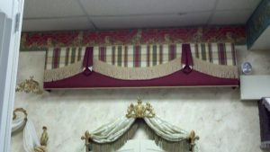 Straight cornice with flat swags and pelmets. Throw swag valance with bullion fringe over arched plantation shutters.